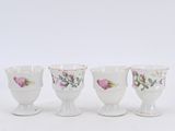 four white cups with pink flowers are lined up on a white surface