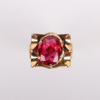 un gros plan d'une bague en pierre rouge posée sur une surface blanche