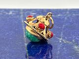une bague en or ornée d'une perle verte et rouge sur un fond bleu