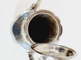 a silver tea pot and a silver spoon on a table