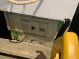 une boîte blanche surmontée d'une corde, à côté d'un poteau jaune