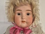 a doll with blonde hair wearing a white dress and a pink bow