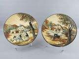 two decorative plates with a painting of a village scene on them