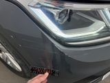 the front of a car with a person ' s hand on the front of it and a sticker on the front of the headlight of the car