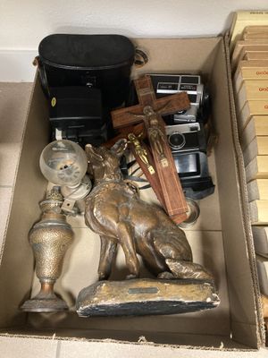une boîte remplie d'objets divers, parmi lesquels un appareil photo, une horloge et une statuette