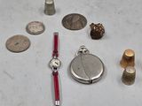 une montre en argent, un bracelet rouge, une montre en argent et une pièce en argent posés sur une surface blanche