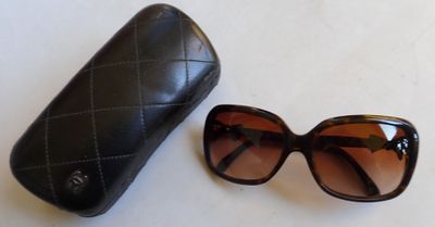 une paire de lunettes de soleil et son étui posés sur une surface blanche, sur fond blanc