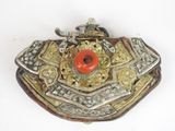 a silver and gold brooch with a red stone in it