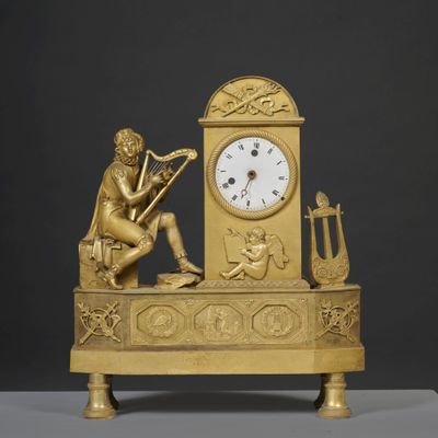 a gold clock with a man playing a musical instrument