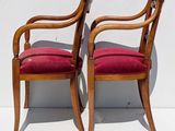 two wooden chairs with red upholstered cushions against a white wall