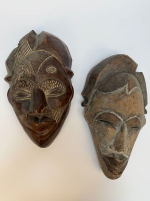 deux masques en bois posés sur une surface blanche, sur fond blanc