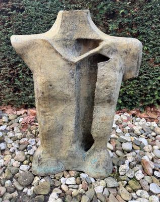 une sculpture en pierre représentant le torse d'un homme, au milieu d'une aire de gravier
