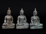 trois statues de Bouddha en bronze, assises en rang sur un fond noir