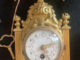 a gold clock hanging on the wall with a chain