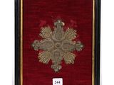 a framed picture of a gold cross on a red velvet background
