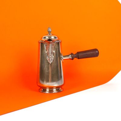 une cafetière en argent avec une poignée en bois sur fond orange