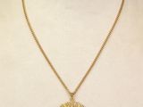 a woman wearing a gold necklace with a sun pendant on it