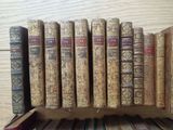 several old books are stacked on a wooden shelf on a table