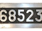 une plaque métallique sur laquelle figure un numéro, sur fond blanc