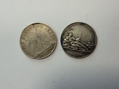 two silver coins sitting next to each other on a white surface