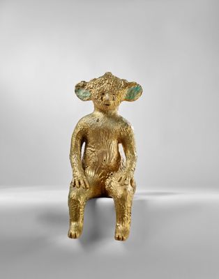 une figurine en or représentant un singe assis sur une surface blanche