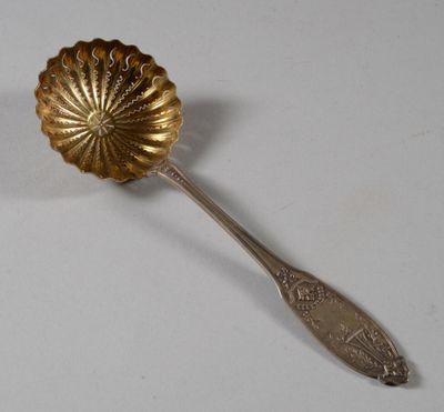 une cuillère en argent ornée d'une fleur sur une surface blanche