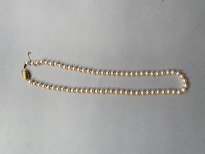 un gros plan d'un collier de perles dorées posé sur une surface blanche