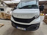 La camionnette blanche est garée dans un entrepôt où se trouvent des palettes et des cartons.