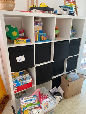 une bibliothèque blanche sur laquelle sont posés des bacs noirs et des jouets