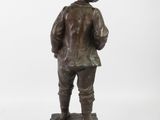 bronze statue of a man with a hat and jacket on a wooden base