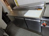 un plan de travail en acier inoxydable dans une cuisine professionnelle, sur lequel est posé une planche à découper