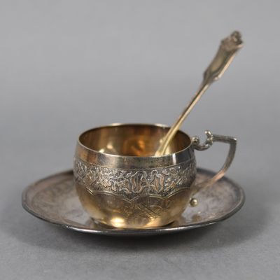 une tasse et une soucoupe anciennes en argent, avec une cuillère posée sur la soucoupe