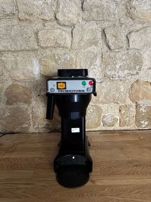 une cafetière posée sur un parquet, près d'un mur en pierre