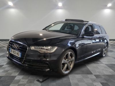 L'Audi break noire est garée dans une grande pièce au sol carrelé en damier.