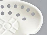 a white bowl with holes in it on a gray surface