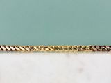 Le bracelet en chaîne d'or est posé sur une dalle de marbre.
