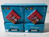 Voici deux boîtes de Rubik's de Disney posées sur une surface blanche.