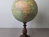 un vieux globe terrestre posé sur un socle en bois, avec un mur blanc en arrière-plan