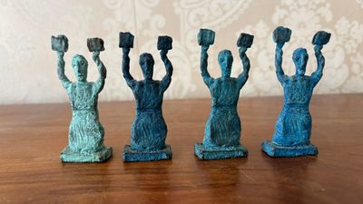 four figurines of women holding up their hands on a wooden table