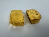 two pieces of gold sitting on top of a white surface