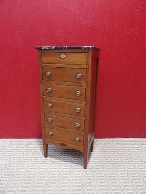 an image of a small wooden chest of drawers against a red wall