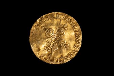 une pièce d'or sur laquelle est gravée une croix, sur fond noir