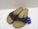 pair of black sandals on a white surface with a price tag