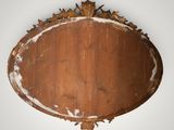 an oval mirror with a wooden frame with a leaf motif
