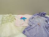trois vêtements de bébé posés sur un lit, à côté d'un ours en peluche