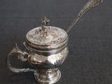 an antique silver teapot with a spoon on a black background