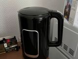 a black coffee pot sitting on top of a desk next to a microwave