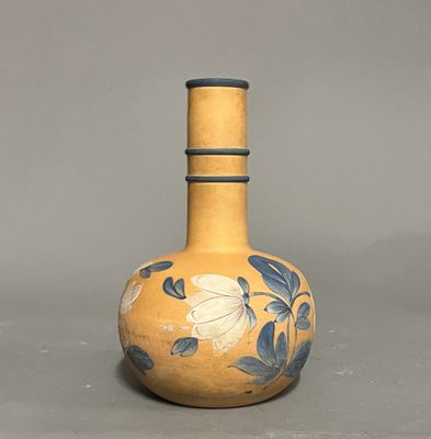 un vase jaune orné de fleurs bleues, posé sur un fond gris