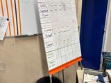 a dry erase board in the corner of a room next to a trash can