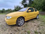 the yellow car is parked in the gravel near the trees